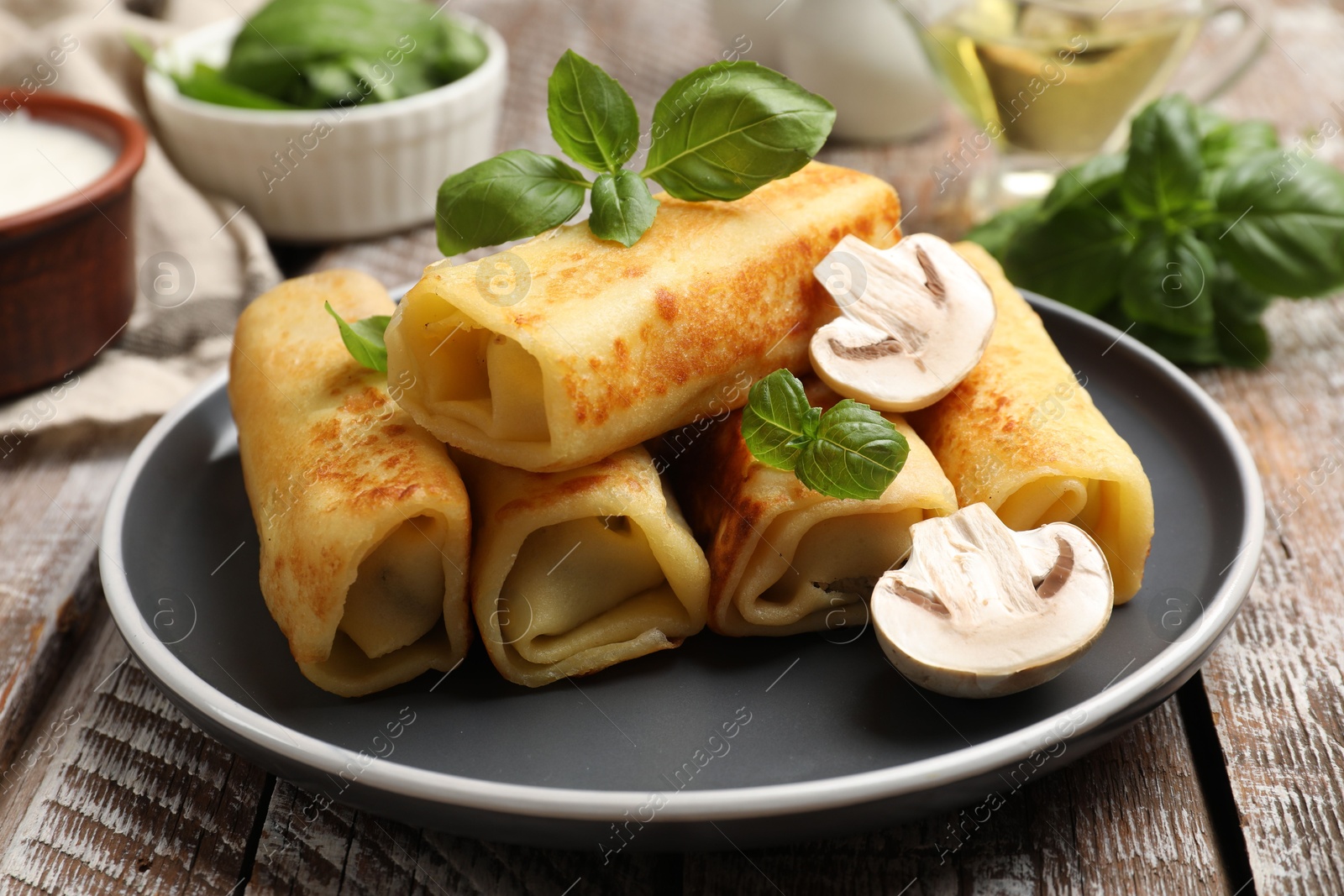 Photo of Delicious rolled crepes with mushrooms and basil on wooden table, closeup