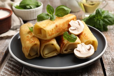 Photo of Delicious rolled crepes with mushrooms and basil on wooden table, closeup