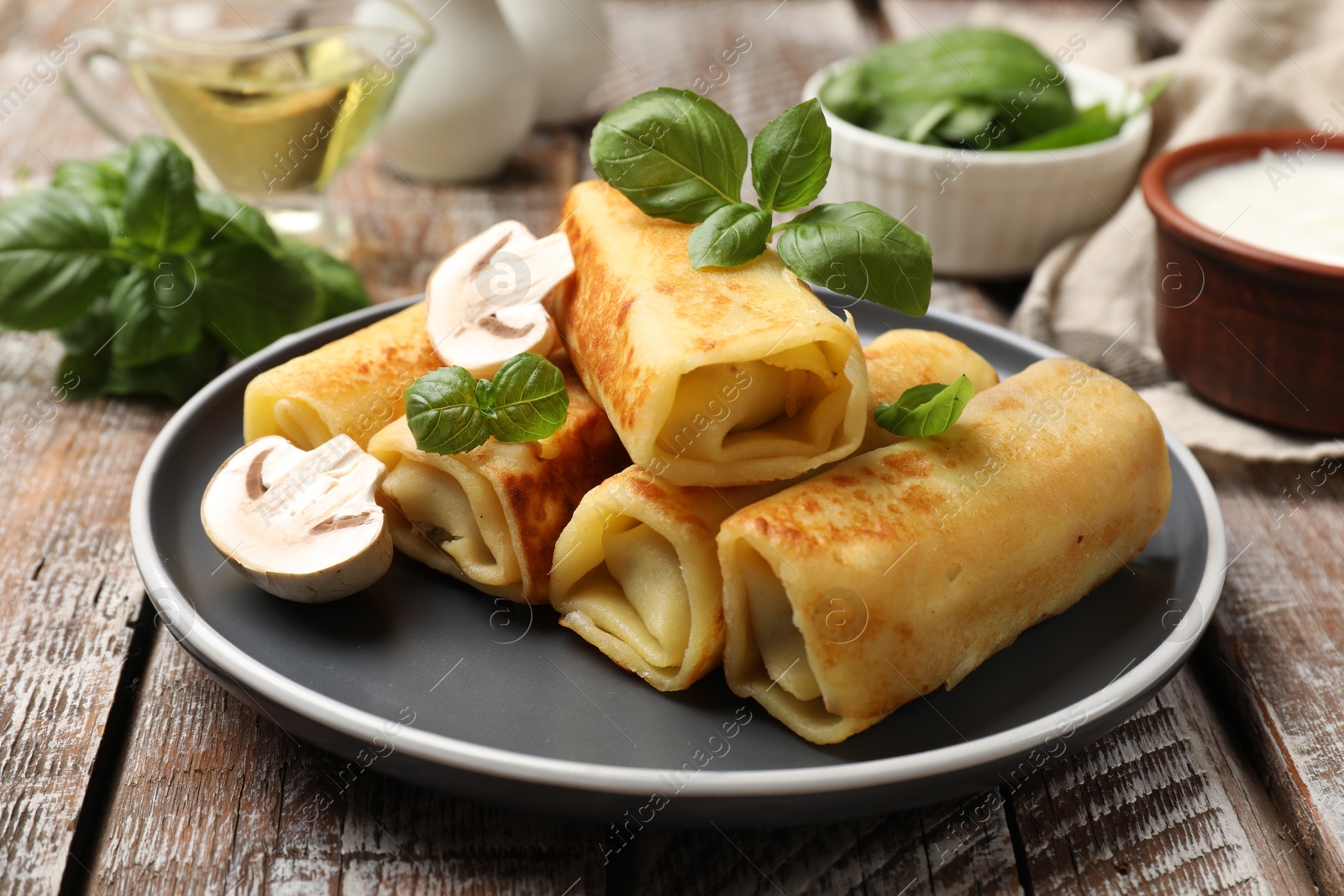 Photo of Delicious rolled crepes with mushrooms and basil on wooden table, closeup