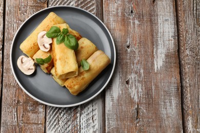 Photo of Delicious rolled crepes with mushrooms and basil on wooden table, top view. Space for text