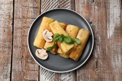 Photo of Delicious rolled crepes with mushrooms and basil on wooden table, top view