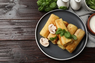 Photo of Delicious rolled crepes with mushrooms, basil and sour cream on wooden table, flat lay. Space for text