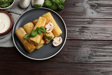 Photo of Delicious rolled crepes with mushrooms, basil and sour cream on wooden table, flat lay. Space for text