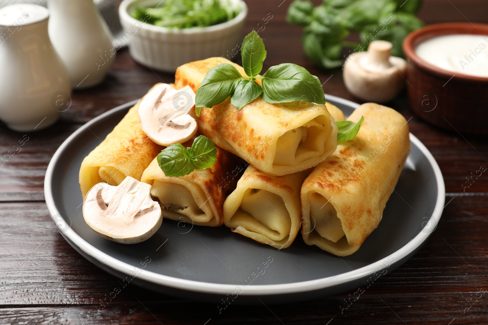 Photo of Delicious rolled crepes with mushrooms and basil on wooden table, closeup