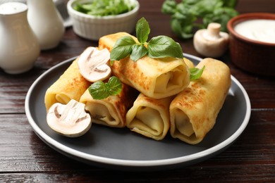 Photo of Delicious rolled crepes with mushrooms and basil on wooden table, closeup