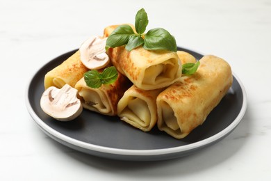 Photo of Delicious rolled crepes with mushrooms and basil on white marble table, closeup