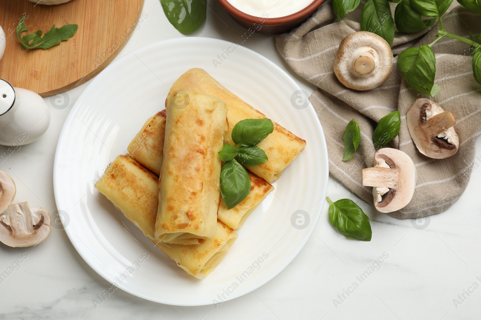 Photo of Delicious rolled crepes with mushrooms and basil on white marble table, flat lay