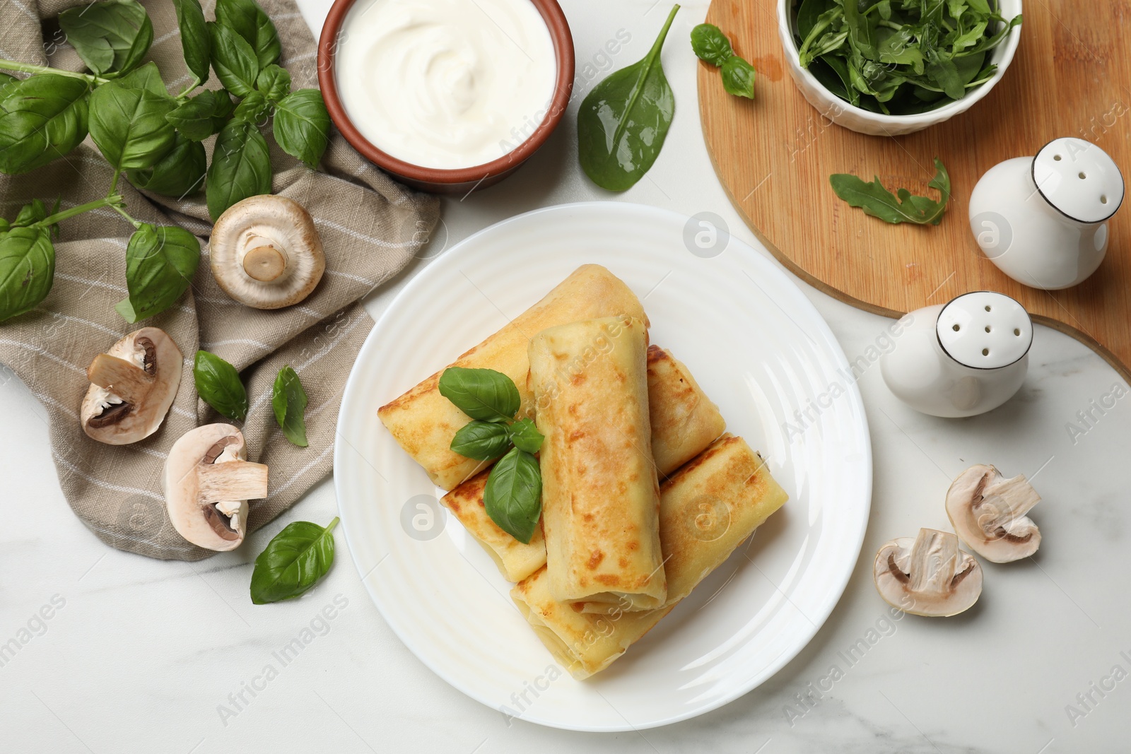 Photo of Delicious rolled crepes with mushrooms, basil and sour cream on white marble table, flat lay