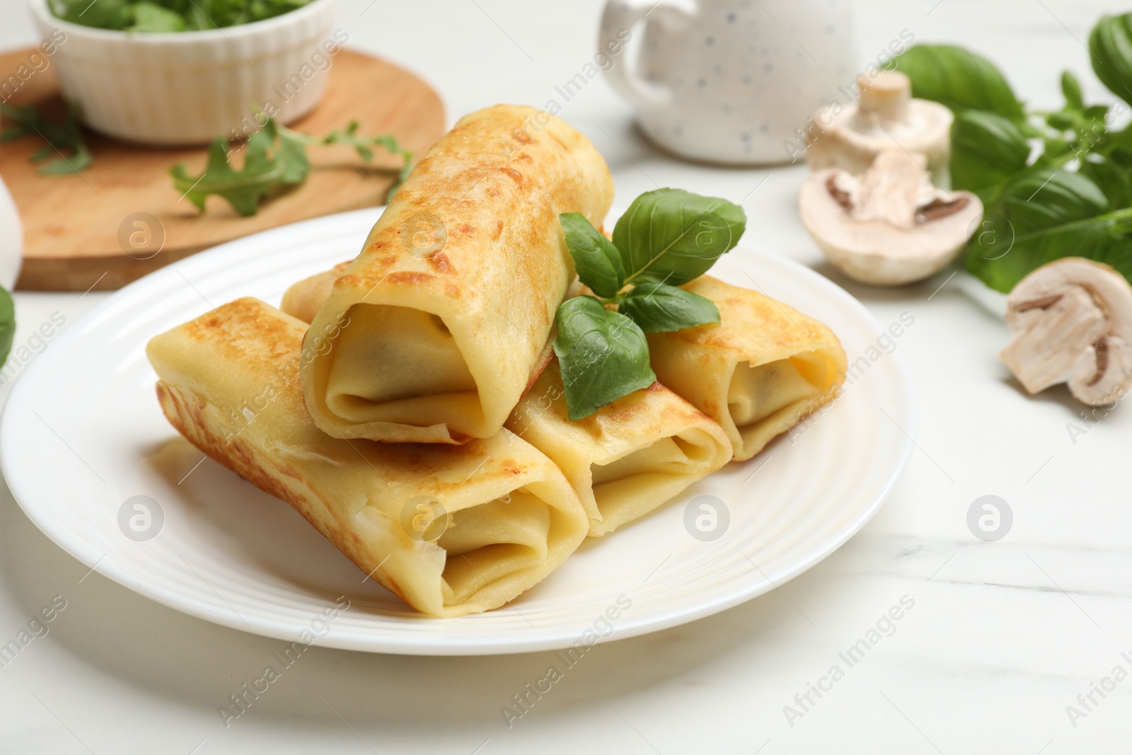 Photo of Delicious rolled crepes with basil and mushrooms on white marble table, closeup