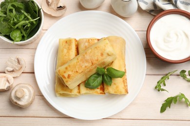 Photo of Delicious rolled crepes with basil, arugula, mushrooms and sour cream on wooden table, flat lay