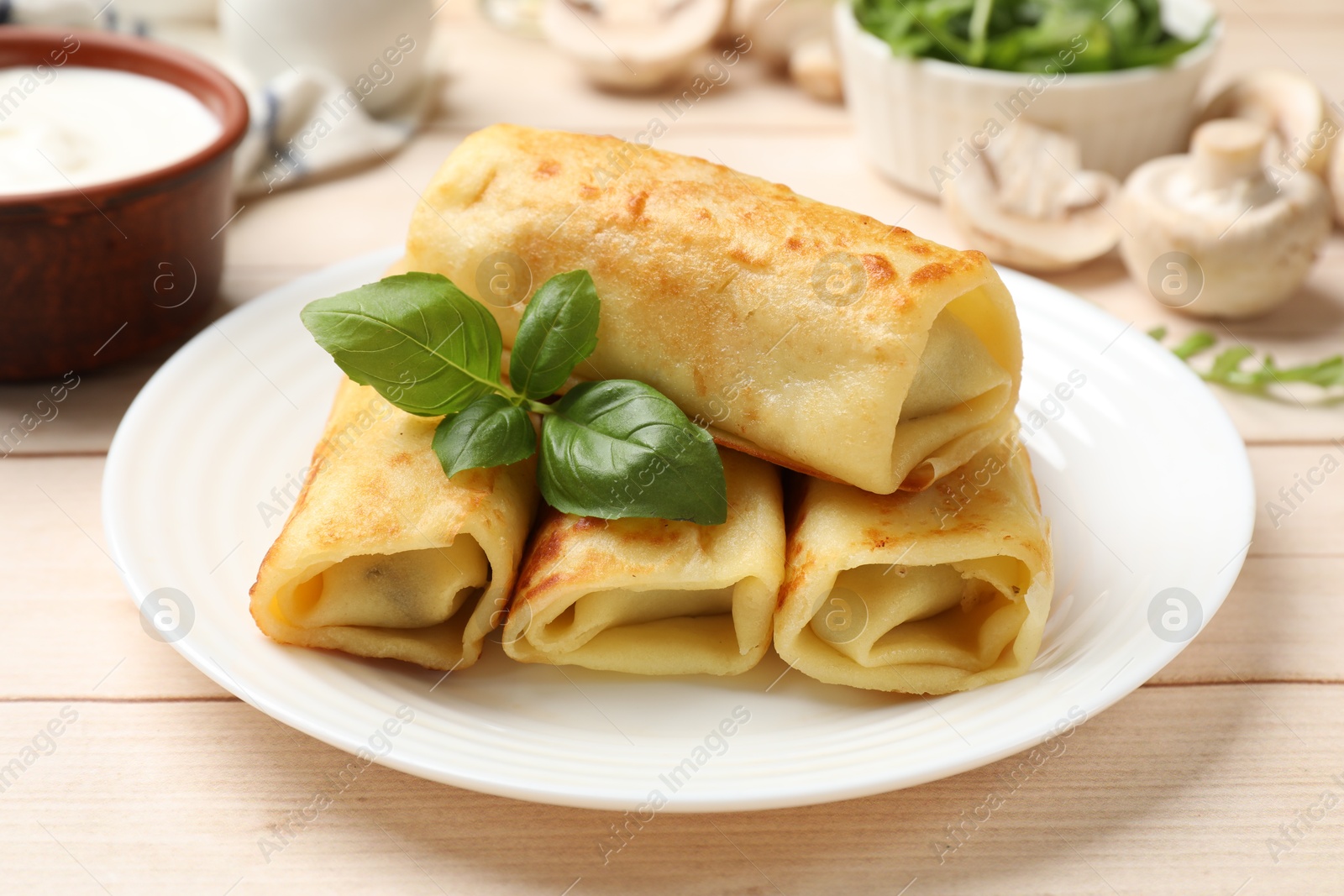 Photo of Delicious rolled crepes with basil, mushrooms and sour cream on wooden table, closeup