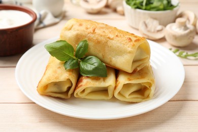 Photo of Delicious rolled crepes with basil, mushrooms and sour cream on wooden table, closeup