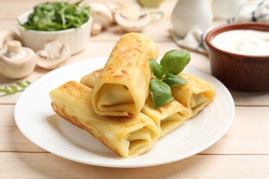 Photo of Delicious rolled crepes with basil, mushrooms and sour cream on wooden table, closeup