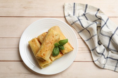 Photo of Delicious rolled crepes with basil on wooden table, top view