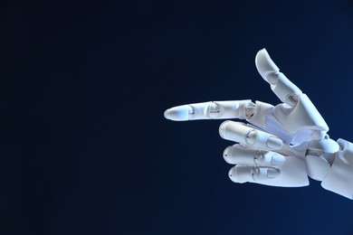 Photo of Artificial intelligence. Robot hand pointing at something on dark blue background, space for text