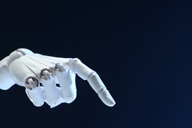 Photo of Artificial intelligence. Robot hand pointing at something on dark blue background, space for text