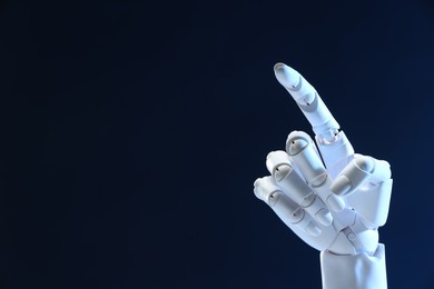 Photo of Artificial intelligence. Robot hand pointing at something on dark blue background, space for text