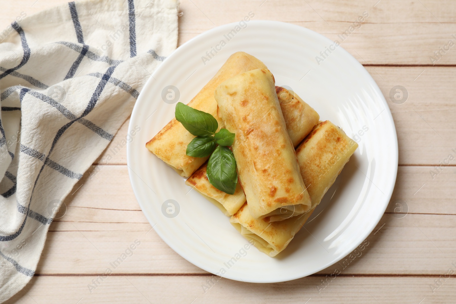 Photo of Delicious rolled crepes with basil on wooden table, top view