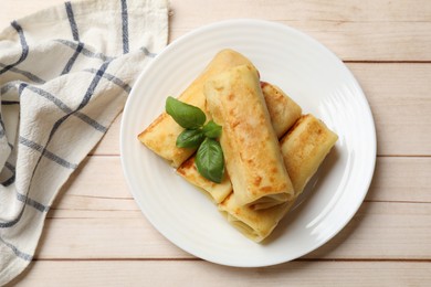 Photo of Delicious rolled crepes with basil on wooden table, top view