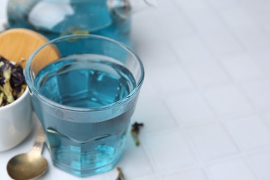 Delicious butterfly pea flower tea on white tiled table, closeup. Space for text