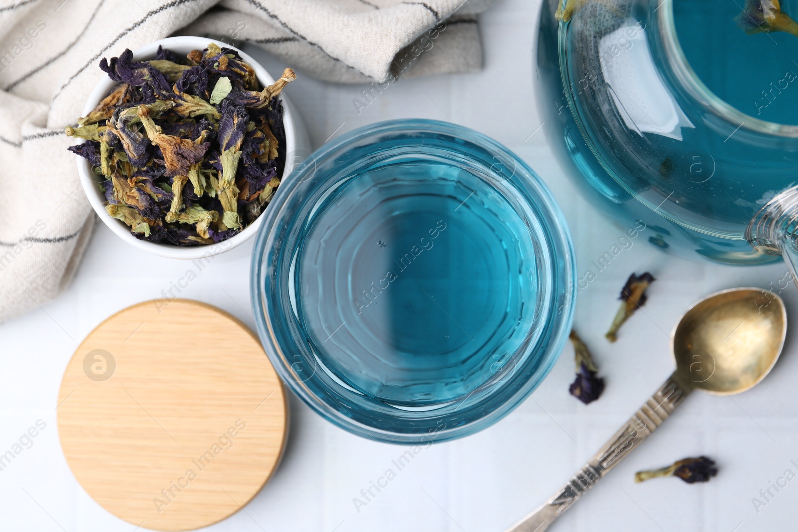 Photo of Delicious butterfly pea flower tea on white tiled table, flat lay