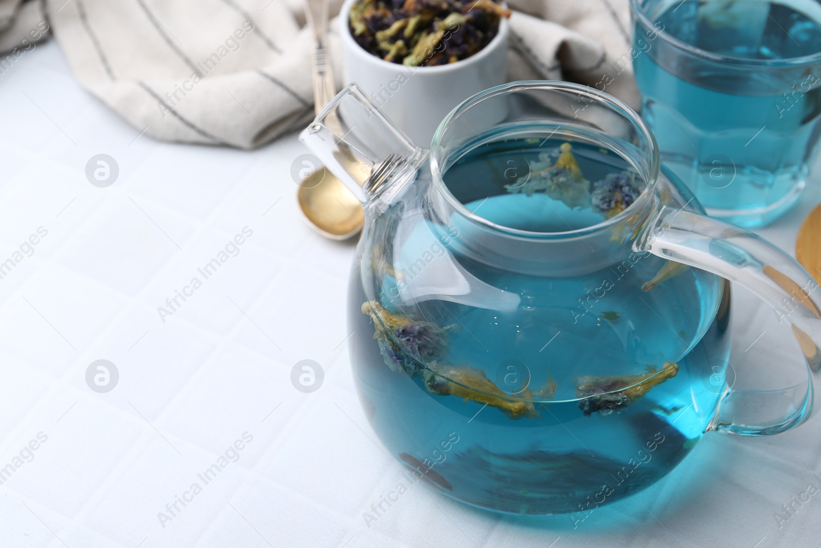 Photo of Delicious butterfly pea flower tea on white tiled table, closeup. Space for text