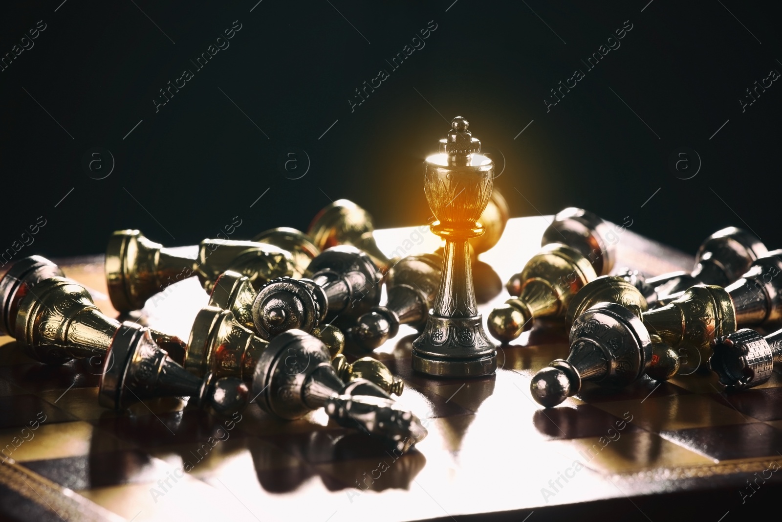 Image of Glowing king standing among lying chess pieces on wooden chessboard