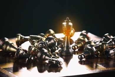 Image of Glowing king standing among lying chess pieces on wooden chessboard