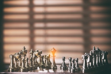 Image of Glowing queen standing among other chess pieces on wooden chessboard in room