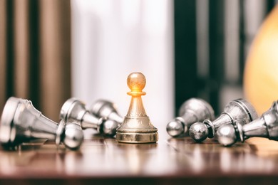 Image of Glowing pawn standing among bowing others on wooden chessboard indoors