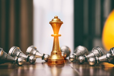 Image of Golden queen standing among bowing pawns on wooden chessboard indoors