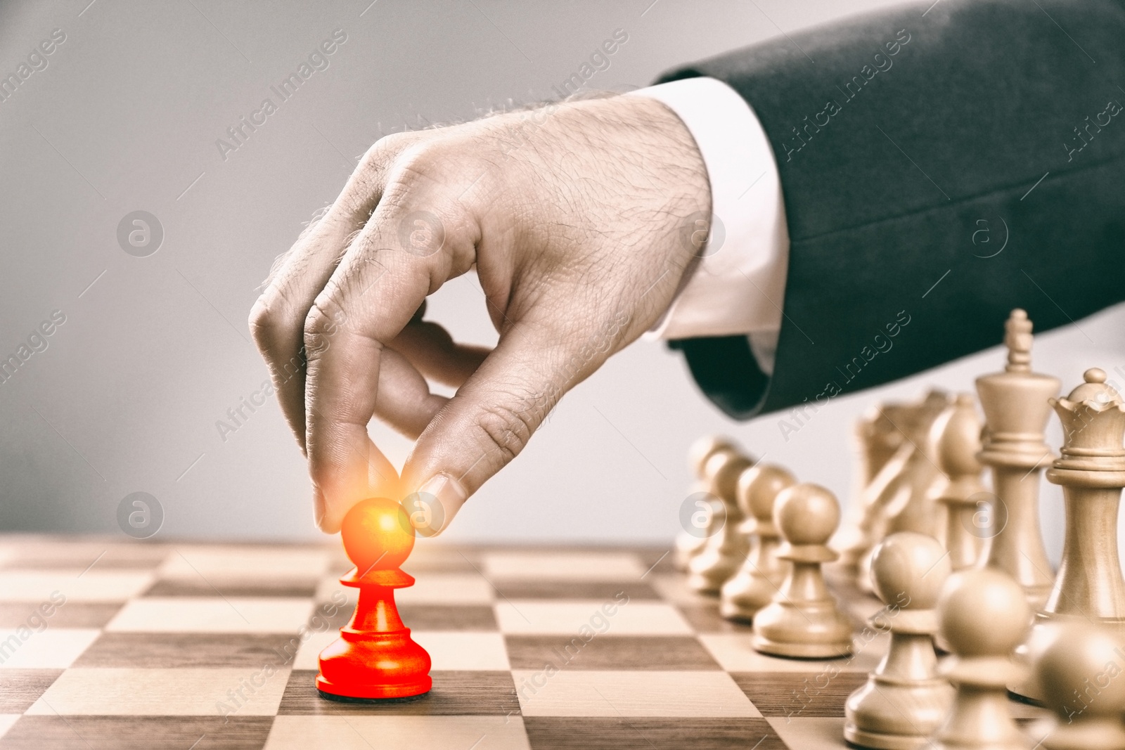 Image of Man making first move by placing red pawn on wooden chessboard, closeup