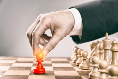 Image of Man making first move by placing red pawn on wooden chessboard, closeup