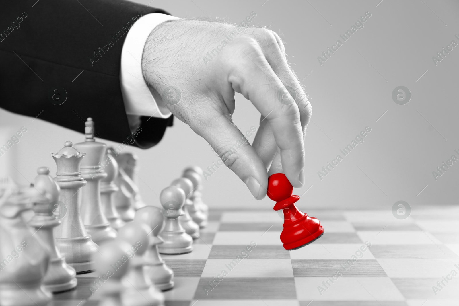 Image of Man making first move by placing red pawn on chessboard, closeup. Black and white effect