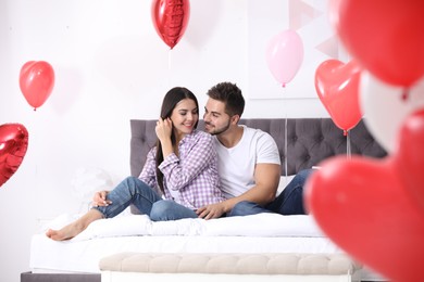 Photo of Lovely young couple in bedroom decorated with heart shaped balloons. Valentine's day celebration