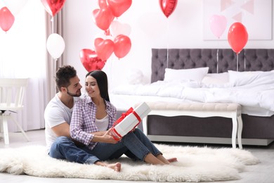 Happy young couple in bedroom decorated with heart shaped balloons. Valentine's day celebration