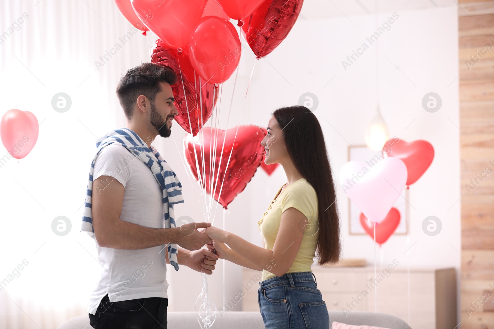 Photo of Happy young couple with heart shaped balloons in living room. Valentine's day celebration