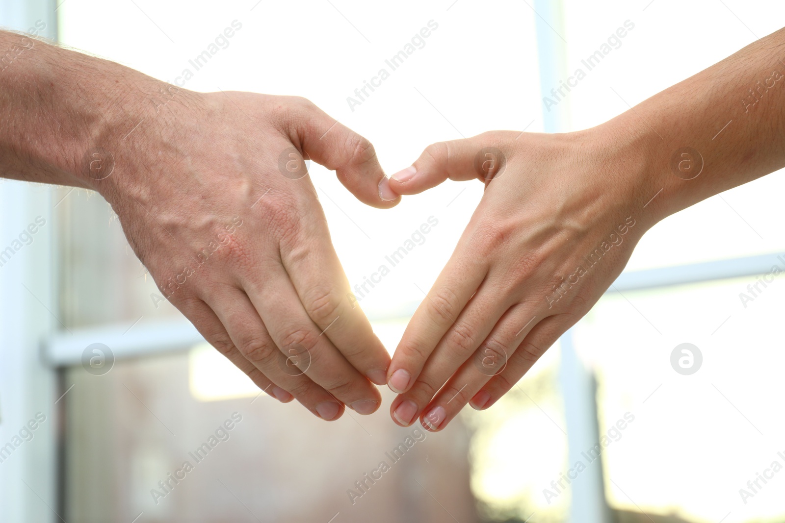 Photo of Young people forming heart with hands indoors, closeup. Happy family