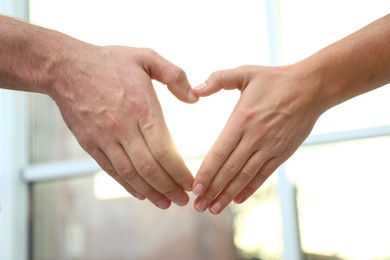 Photo of Young people forming heart with hands indoors, closeup. Happy family