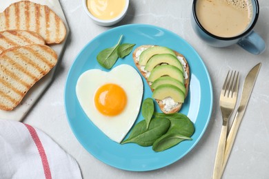 Photo of Romantic breakfast with heart shaped fried egg served on light grey table, flat lay