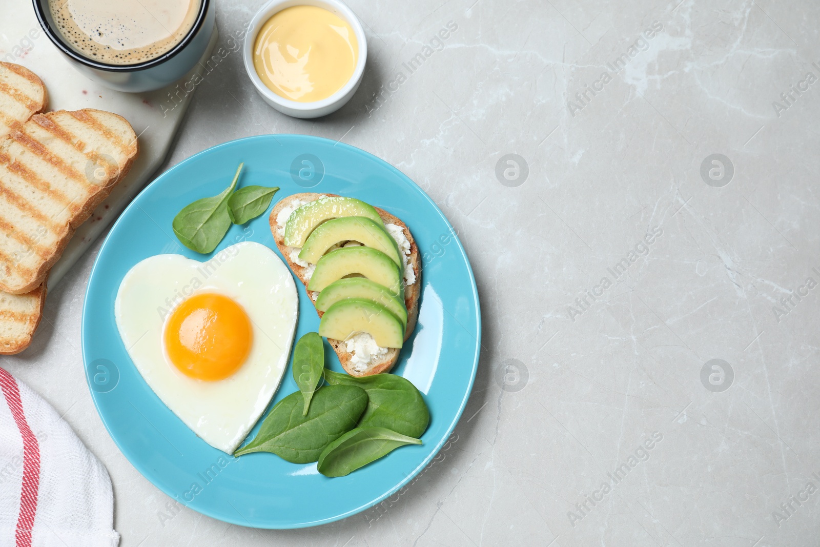 Photo of Romantic breakfast with heart shaped fried egg served on light grey table, flat lay. Space for text