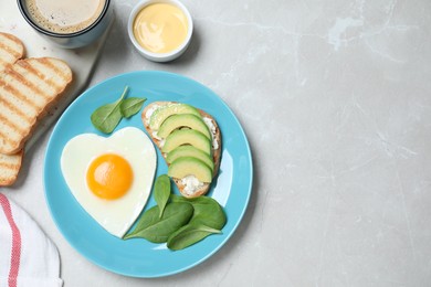 Photo of Romantic breakfast with heart shaped fried egg served on light grey table, flat lay. Space for text