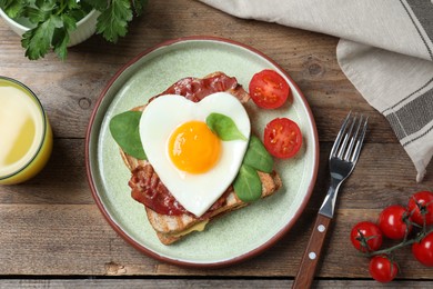 Photo of Tasty sandwich with heart shaped fried egg and bacon on wooden table, flat lay