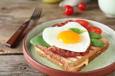 Photo of Plate of tasty sandwich with heart shaped fried egg and  bacon on wooden table, closeup