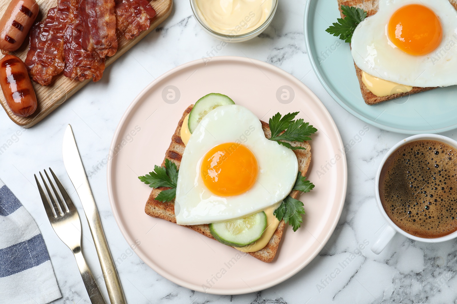 Photo of Tasty sandwiches with heart shaped fried eggs for romantic breakfast on white marble table, flat lay