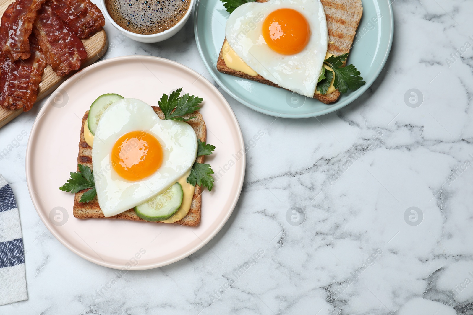 Photo of Tasty sandwiches with heart shaped fried eggs for romantic breakfast on white marble table, flat lay. Space for text