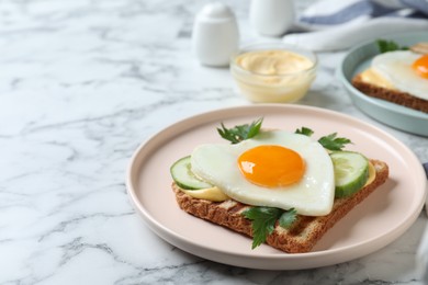 Photo of Plate of tasty sandwich with heart shaped fried egg on white marble table