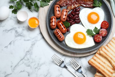 Photo of Delicious breakfast with heart shaped fried eggs and  sausages served on white marble table, flat lay