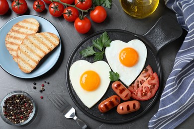 Photo of Delicious breakfast with heart shaped fried eggs and  sausages served on dark grey table, flat lay