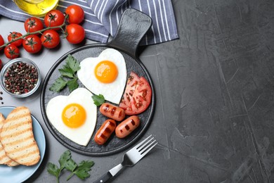 Photo of Delicious breakfast with heart shaped fried eggs and  sausages served on dark grey table, flat lay. Space for text